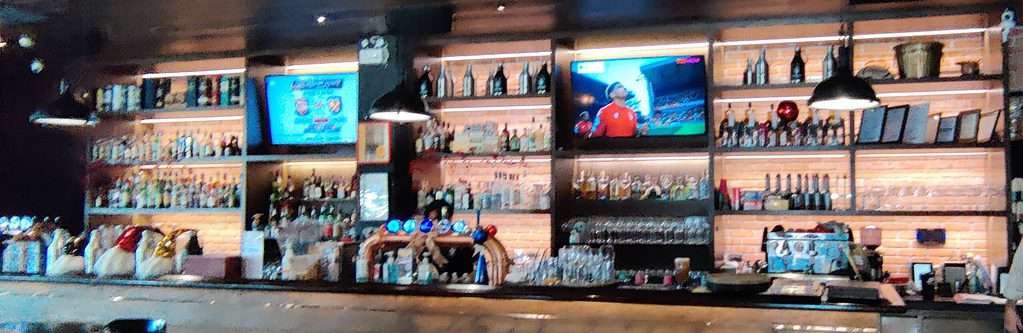 The bar of the Londoner Brew Pub in Bangkok Thailand. Lots of whiskeys, bottles of booze, and two big screens showing international sports. 