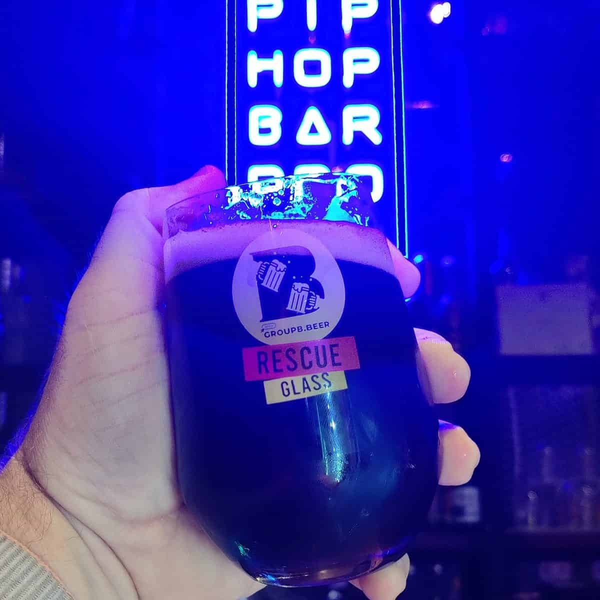 Glass of black IPA in front of Taopiphop's neon sign in Bangkok